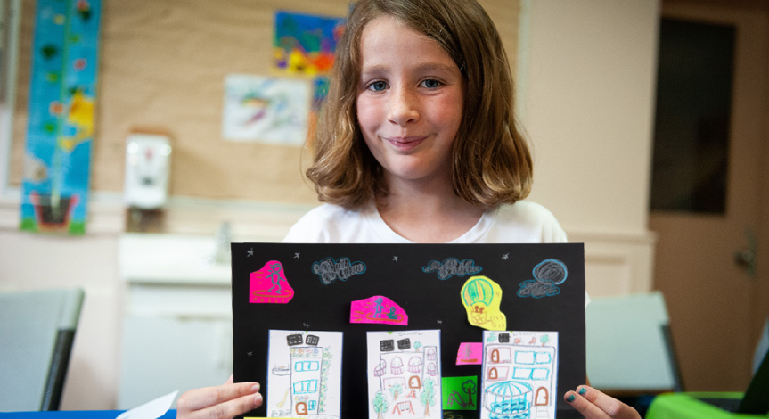 Girl holding a finished art project. The art project is on black construction paper.